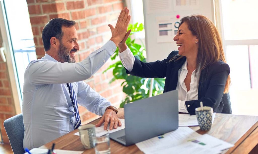 2 business people high-fiving in the office in front of a laptop